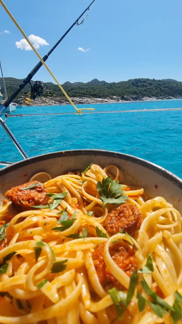 Pâtes à la sauce corse servies à bord avec canne à pêche et eau cristalline en arrière-plan