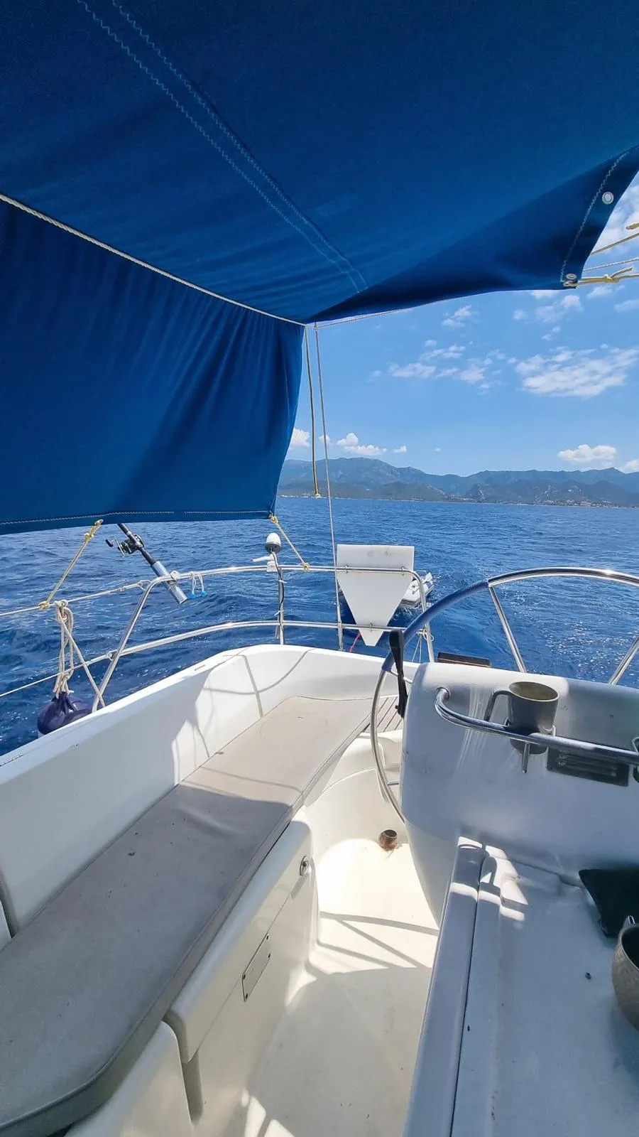 Voile hissée et pont du voilier en navigation face aux montagnes corses
