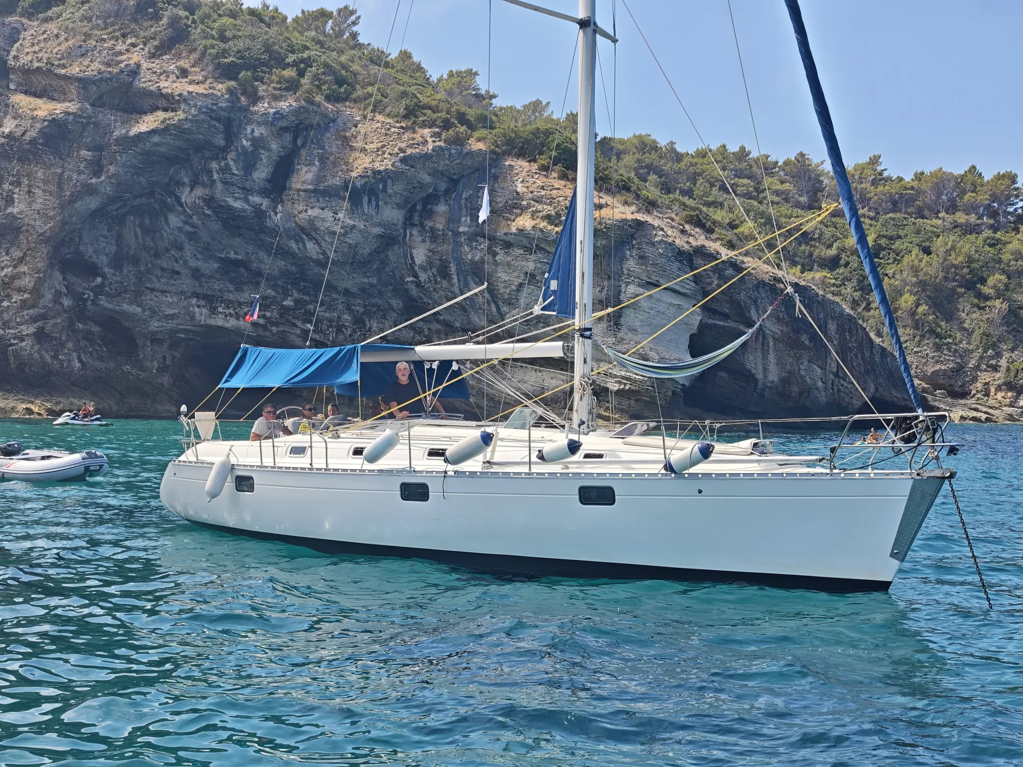 Voilier ancré aux grottes aux pigeons sur le Cap Corse avec l'équipage et les invités à bord, falaise minérale et eau turquoise