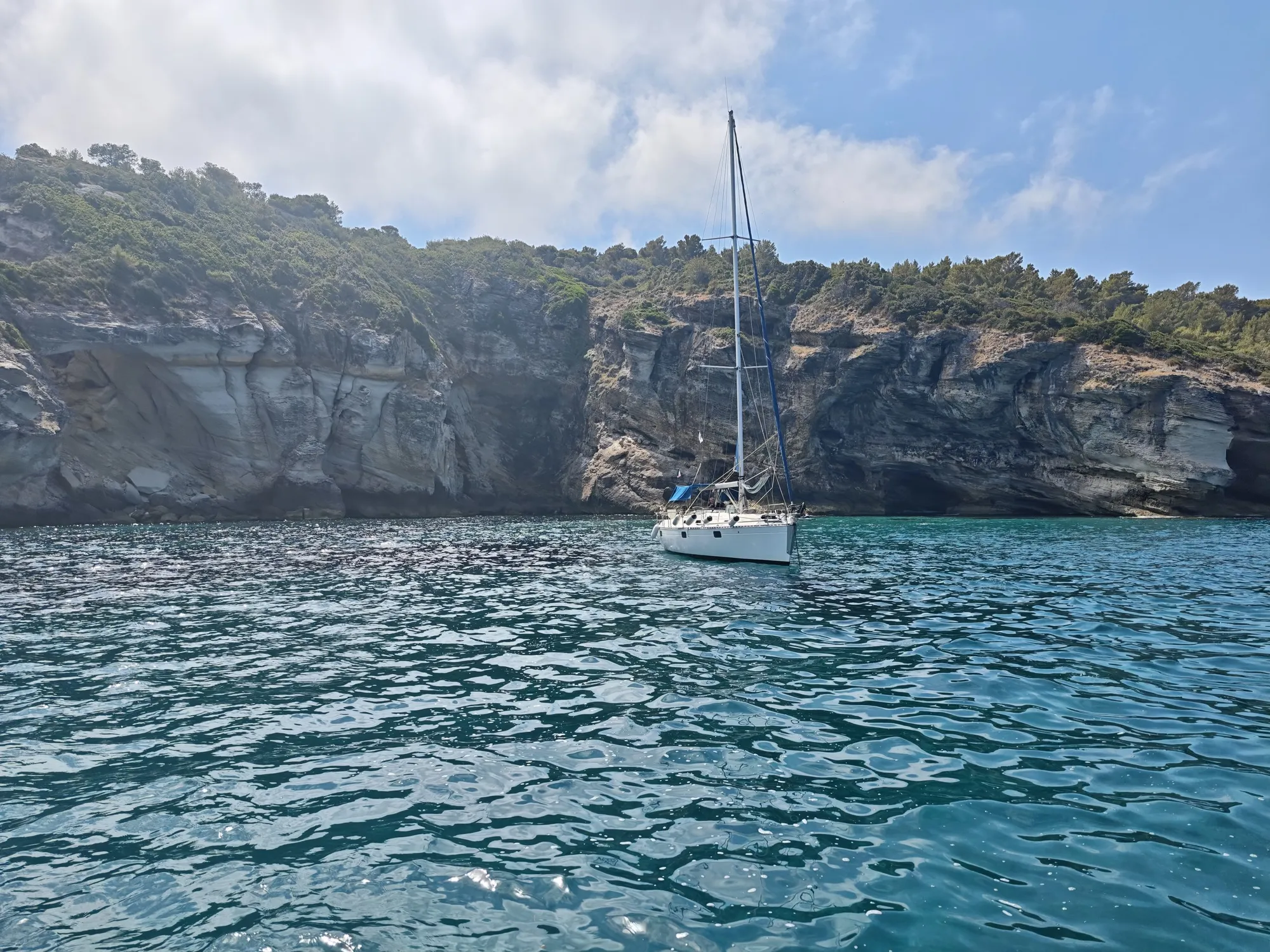 Voilier Eridu au mouillage face aux grottes aux pigeons sur le Cap Corse, eau turquoise cristalline en Haute-Corse